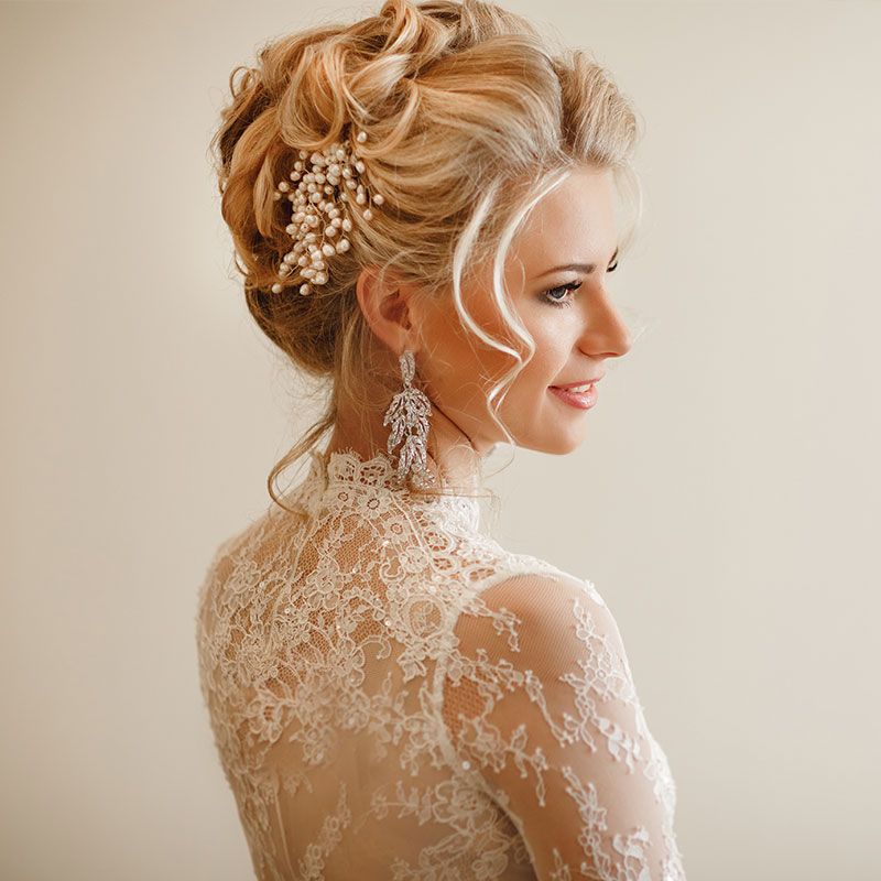 Braut mit eleganter Hochsteckfrisur, Perlen-Haarschmuck und Spitzenkleid im Profil.