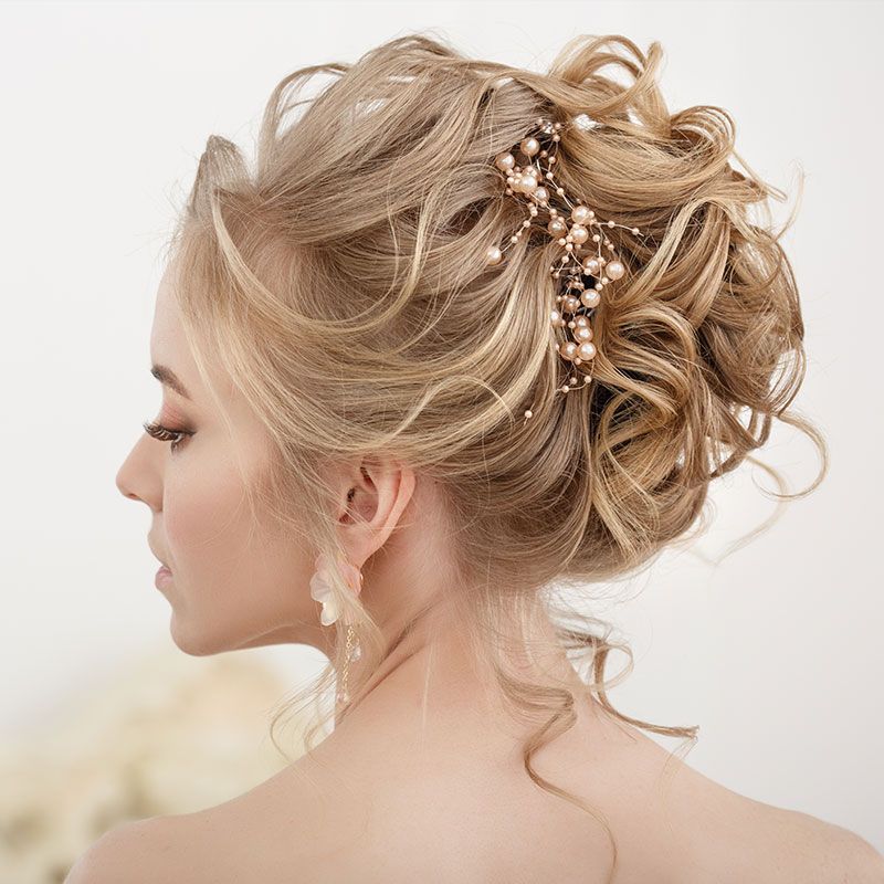 Frau mit elegant hochgesteckter, gelockter Hochzeitsfrisur und Perlen-Haarschmuck.