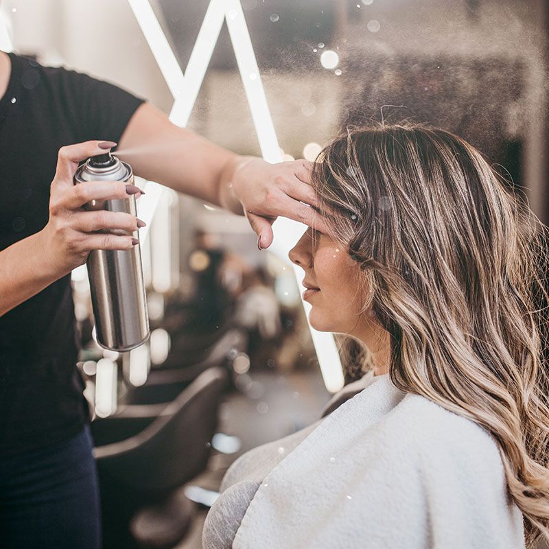 Friseurin sprüht Haarspray auf das gestylte Haar einer Kundin im Salon.